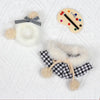 A set featuring a black and white grid cape and beret with fluffy trim and a colorful grid-patterned disc.