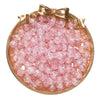 A round dish filled with pink glass crackle beads for jewelry making, tied with a gold bow.