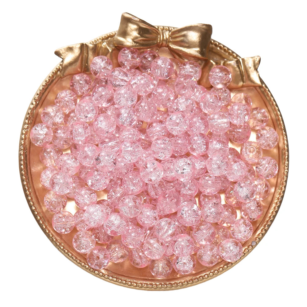 A round dish filled with pink glass crackle beads for jewelry making, tied with a gold bow.