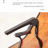 A black ergonomic radian design guitar capo set with picks and holder placed on a wooden surface.
