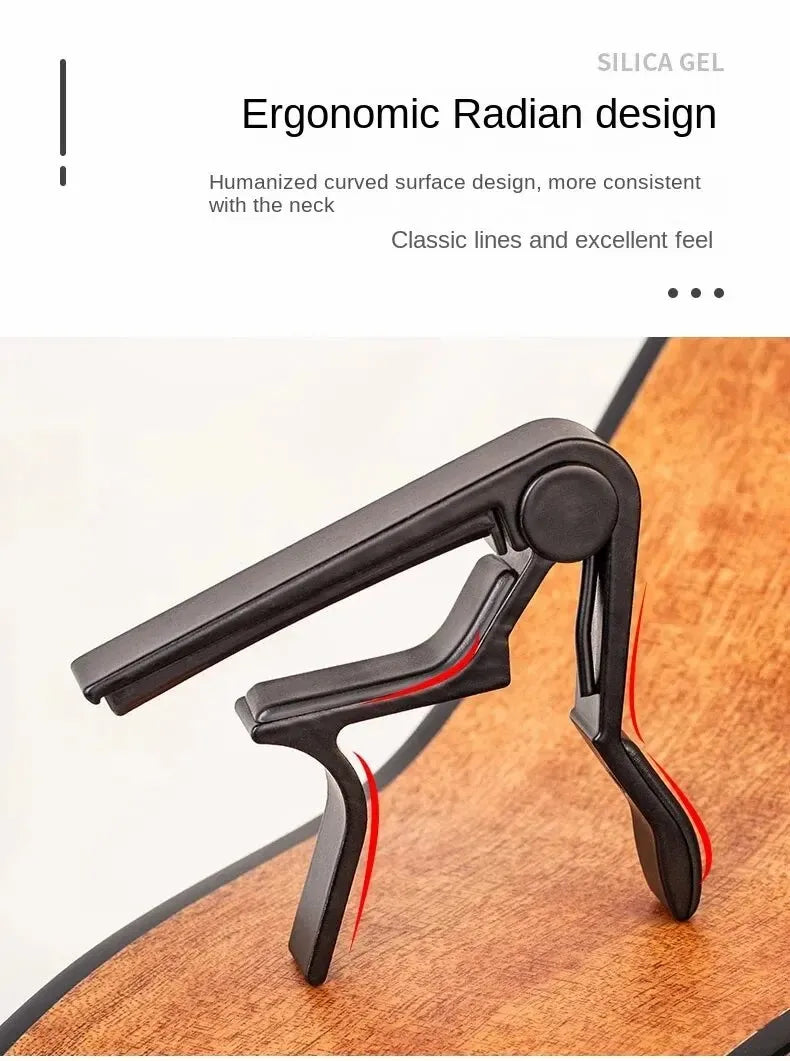 A black ergonomic radian design guitar capo set with picks and holder placed on a wooden surface.