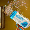 A hand holds a white and blue rocket boom bubble gun spraying bubbles against a yellow background.