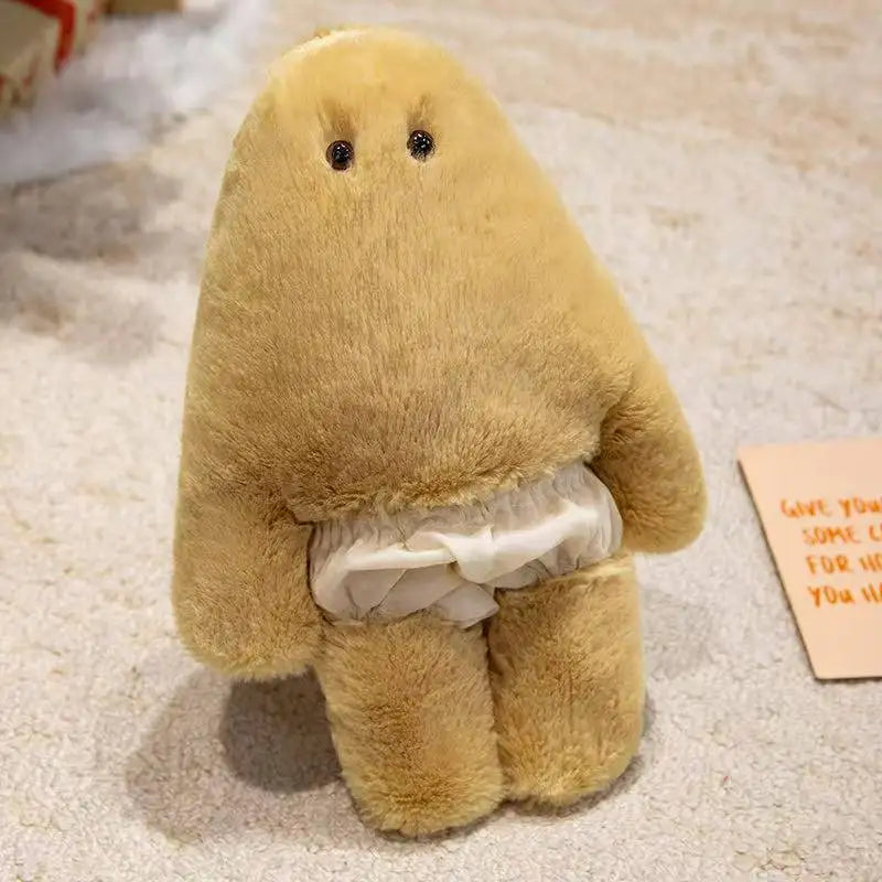 A soft, tan monster plush doll with a light-colored ruffled pant detail is shown on a light background.