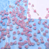 A pile of pink and clear glass beads resembling lily of the valley flowers scattered on a blue surface with a gold stringing 