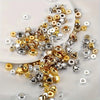 A collection of mixed color acrylic spacer beads in gold silver and clear tones scattered on a white surface.