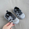 A hand holds a pair of gray and black breathable mesh toddler walking shoes with an anti-slip sole.