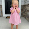 A toddler girl wearing a pink gingham A-line dress with a Peter Pan collar standing outdoors.