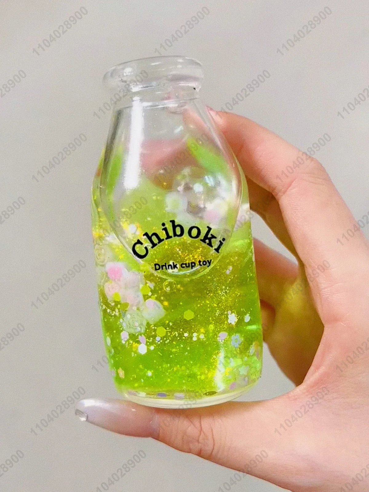 A hand holds a clear bottle filled with bright green liquid, labeled Chiboki Drink cup toy.