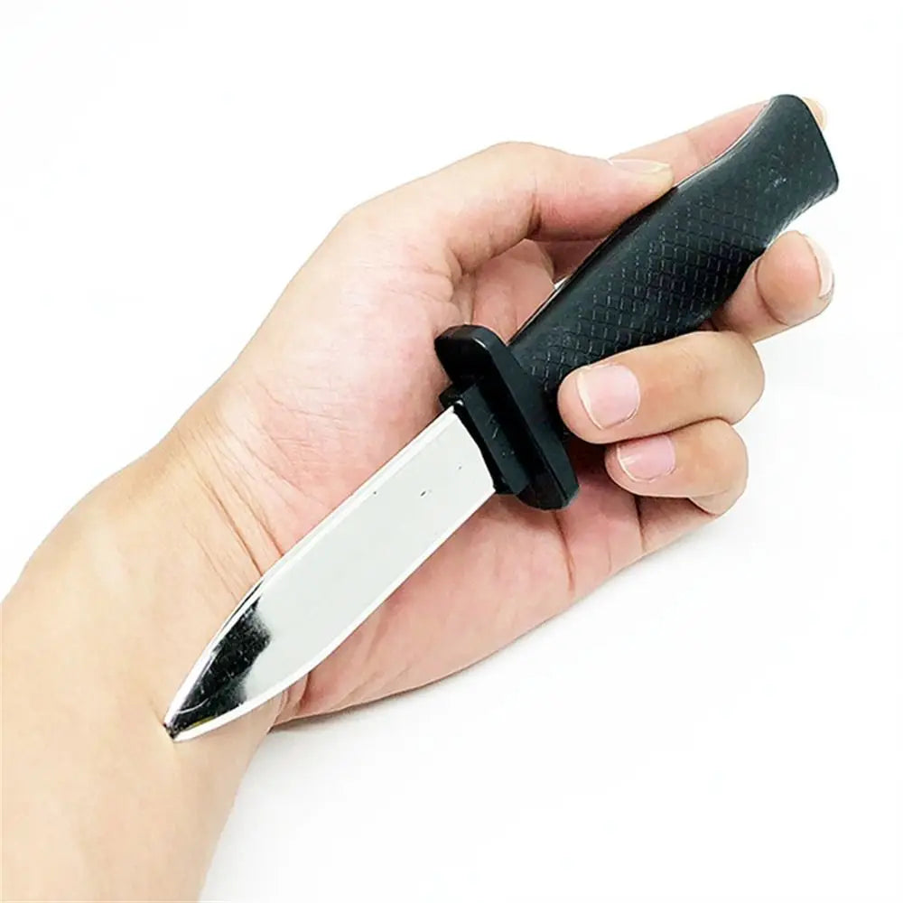 A hand holds a black retractable trick dagger prop knife with a silver blade.