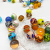 Collection de billes en verre colorées faites à la main, éparpillées sur une surface transparente et texturée.