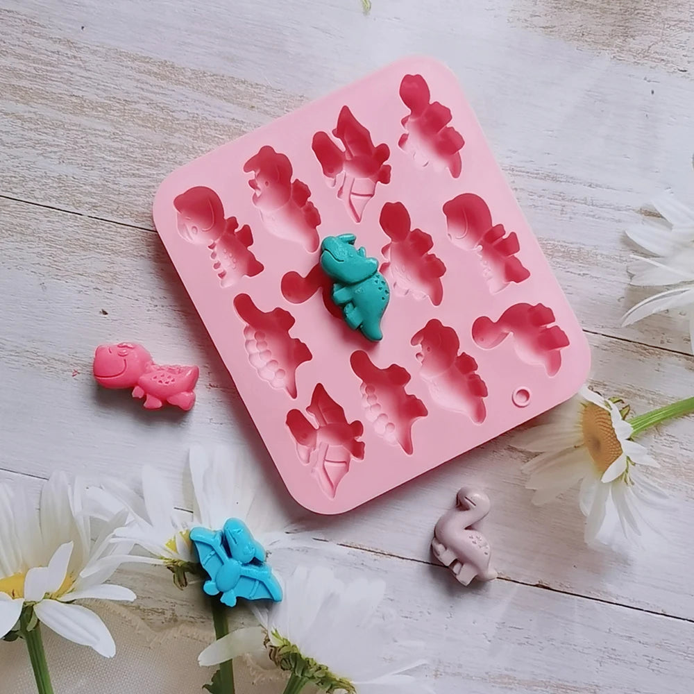 A pink silicone mold with dinosaur shapes is shown on a white wooden surface, surrounded by small colored dinosaurs.