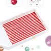 A white tray filled with numerous red round diamonds arranged in rows, demonstrating the size of the stones.