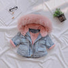 A light blue denim jacket with a pink faux fur collar is displayed on a white sheet.