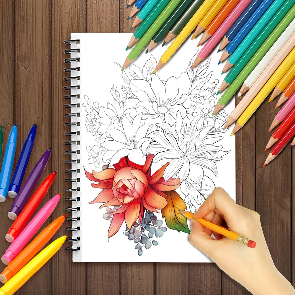 A hand draws a detailed rose and floral design in a spiral-bound coloring book surrounded by colored pencils.
