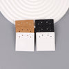 A display of square jewelry cards in kraft brown, black, and white, arranged on a gray surface.