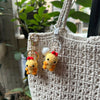 A handmade crochet yellow animal keychain with red accents hanging from a white knitted bag.