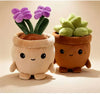 Two plush toys resembling potted succulents, one purple and one green, sitting on a light surface.