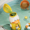 A yellow duck bath toy with an open lid is floating in light green water, next to an orange bath toy.