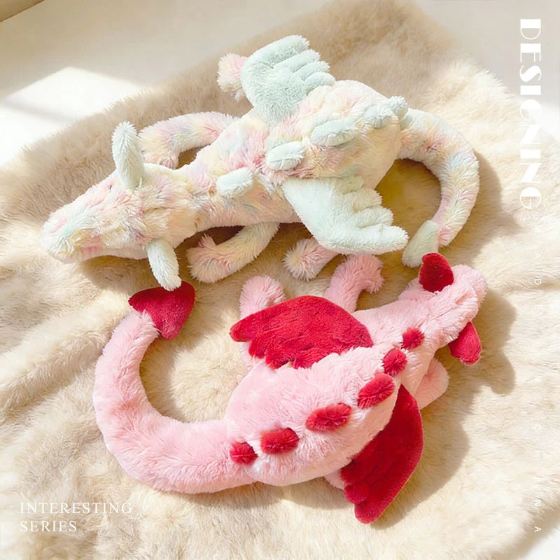 A soft pink and mint green rainbow dragon plush toy lying on a fluffy beige surface.