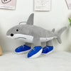 A gray shark plush toy with blue feet is sitting on a white surface.