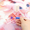 A hand is using a white pen to apply glitter onto a diamond painting surface.
