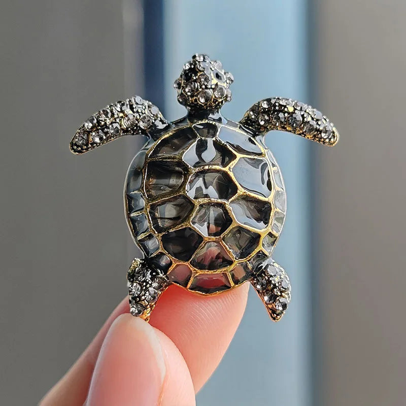 A detailed rhinestone turtle brooch pin with a textured shell and gold accents is held by a hand.