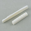 A white real bone guitar nut and bridge saddle shown diagonally on a gray surface.