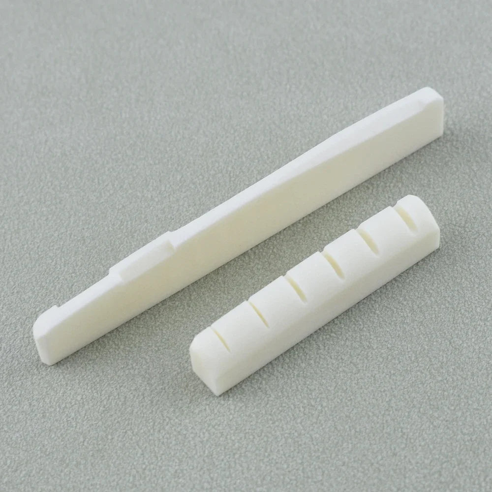 A white real bone guitar nut and bridge saddle shown diagonally on a gray surface.