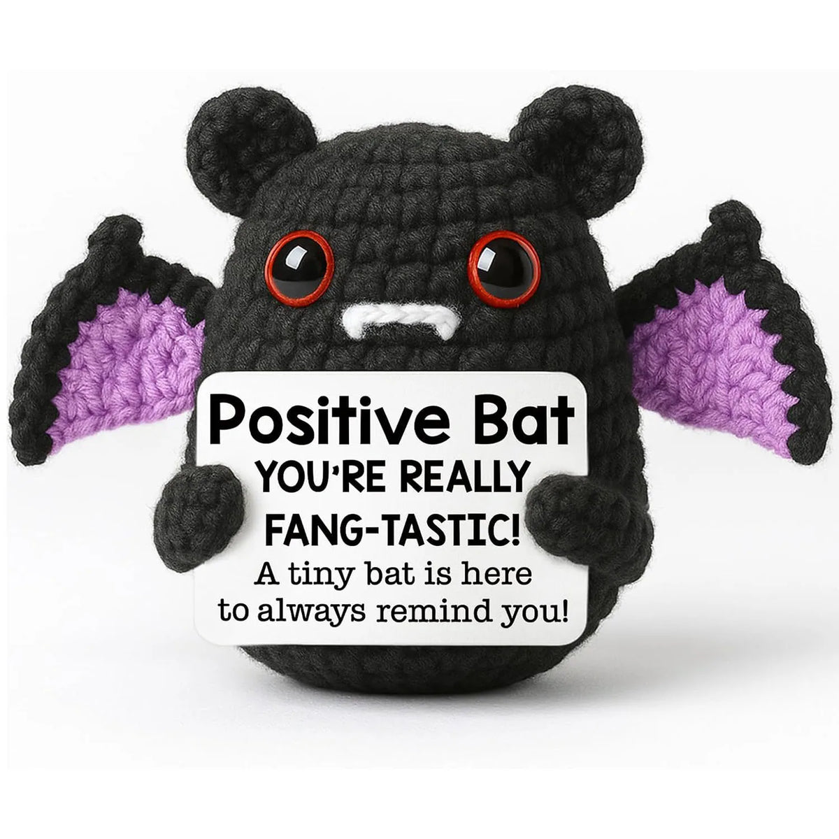 A handmade knitted bat doll with black body, white mouth, and purple ears, featuring a positive message.