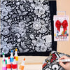 A black and white floral pattern blanket with a pink marker set and other art supplies displayed on a light background.