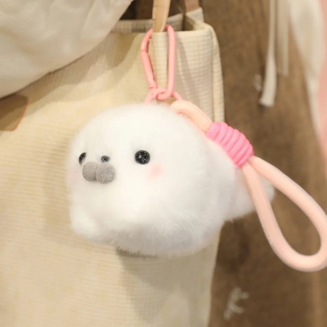 A white seal plush toy with a small gray nose and a pink octopus-themed strap is hanging from a beige bag.