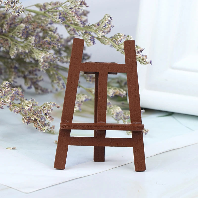 A small, rustic wooden artist easel used as a miniature prop for a dollhouse display.
