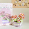 A pink and white miniature flower bouquet building block set displayed next to its packaging.