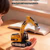 A child's hand holds a yellow mini RC excavator model on a wooden table.