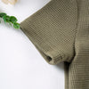 A close-up of a olive green knitted baby outfit set featuring a textured tee and shorts.