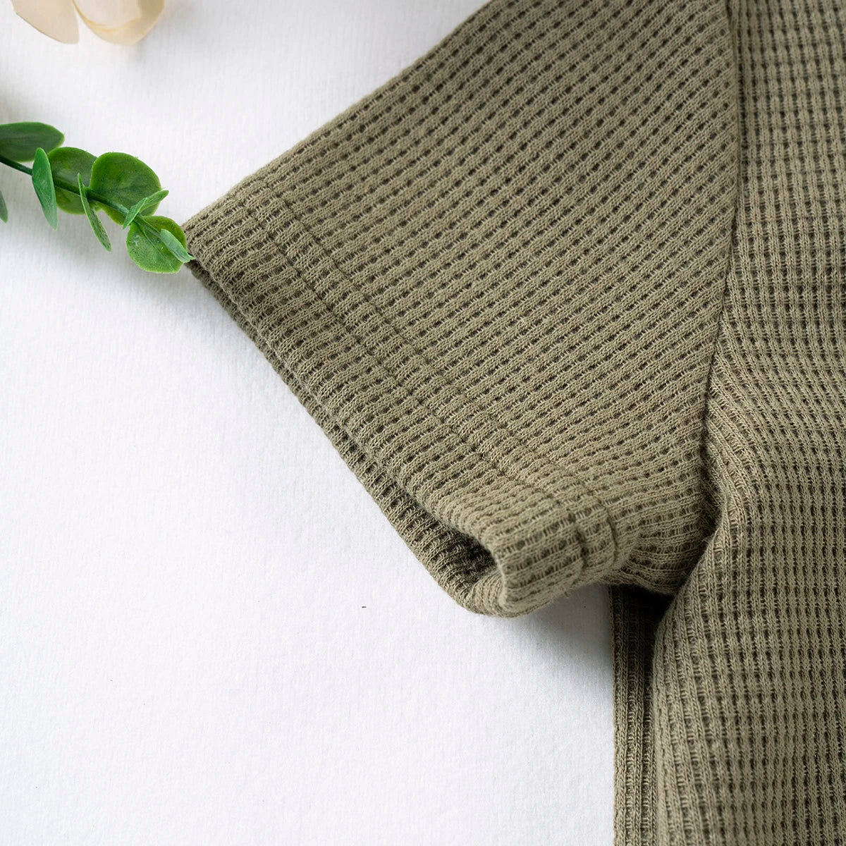 A close-up of a olive green knitted baby outfit set featuring a textured tee and shorts.