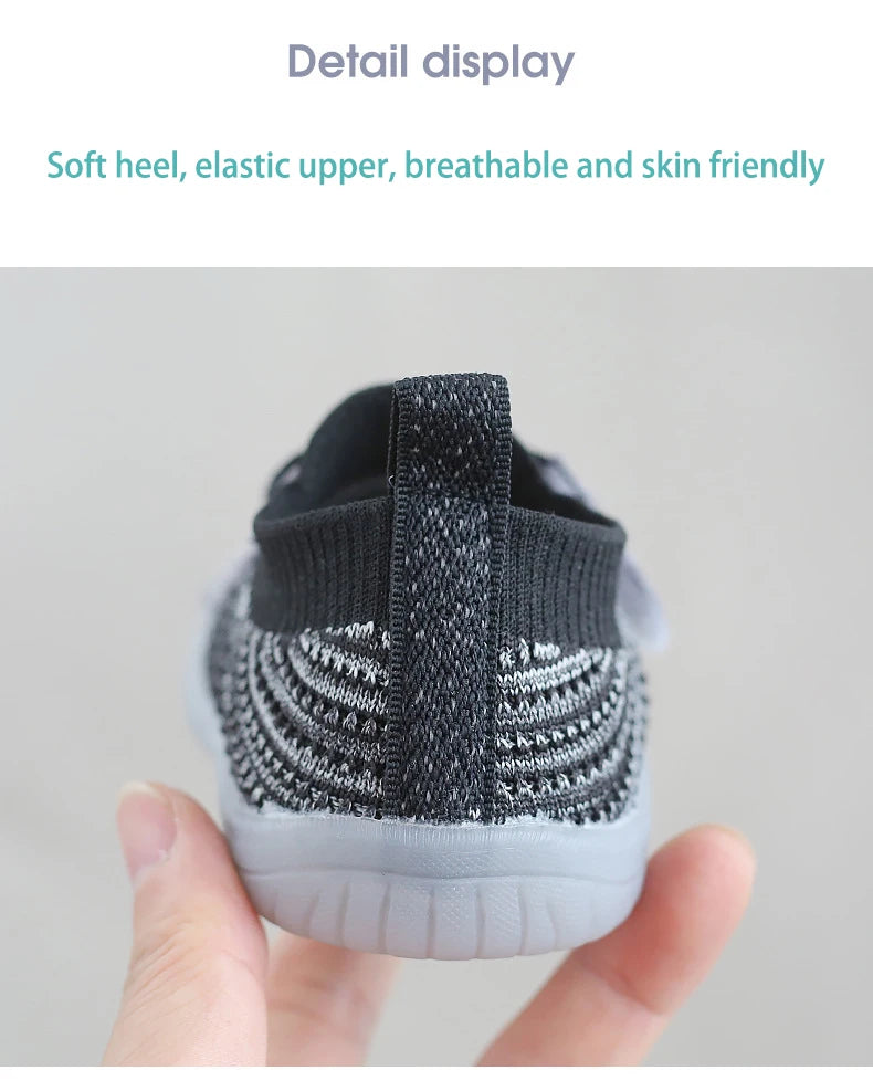 A close-up shot of a pair of black and gray breathable mesh toddler walking shoes being held by a hand.