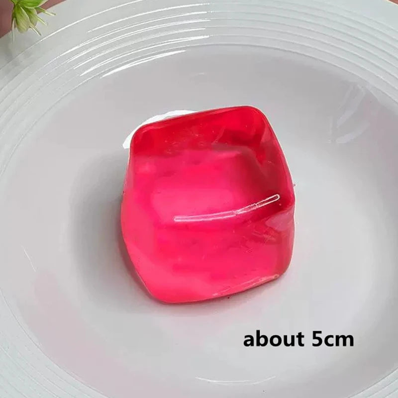 A bright pink, translucent ice cube sensory fidget toy resting in a white bowl.