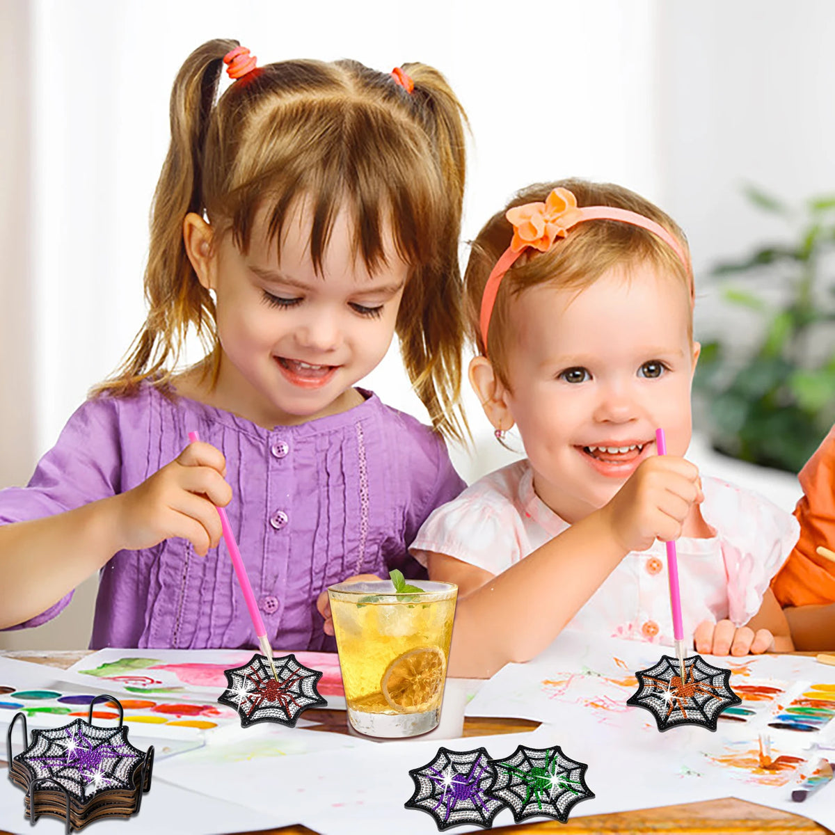 Two young girls are decorating a DIY diamond art coaster set with spider web designs on paper.