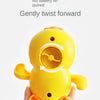 A yellow swimming duck bath toy is gently twisted forward, being held in a person's hand.