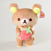 A brown Rilakkuma bear plush toy with yellow ears, holding a pink strawberry accessory.