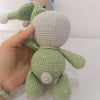 A hand is holding a handmade crochet stuffed bear toy in light green color.