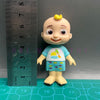 A cute cartoon figurine of a child with yellow hair wearing a blue shirt and shorts, set against a ruler.