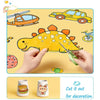 A hand is cutting out a dinosaur shape from yellow sticky coloring paper for decoration.