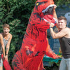 A man is posing with an inflatable red and black T-Rex costume in an outdoor garden setting.