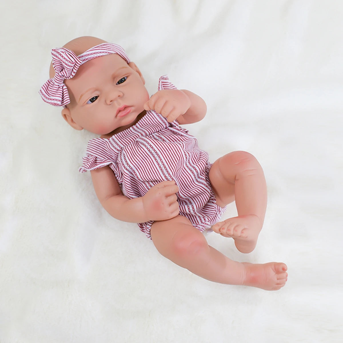 A lifelike vinyl reborn doll with a striped outfit and a matching bow, lying on a white surface.