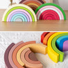 Un ensemble de blocs en bois formant un arc-en-ciel, empilés dans diverses couleurs pastel et vives en demi-cercle.