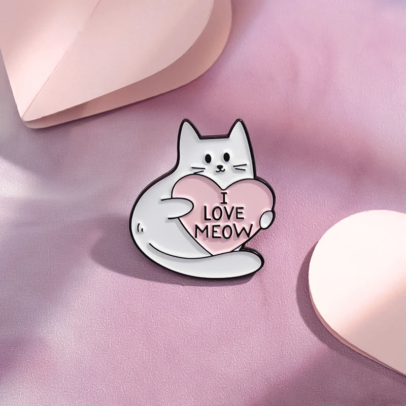 A white cat enamel pin with a pink heart design is placed on a soft pink surface.