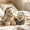 A soft, light brown and white hedgehog plush pillow resting on a cream-colored blanket.