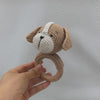 A handcrafted wooden baby rattle and teether ring shaped like a dog, made of light brown and white yarn.